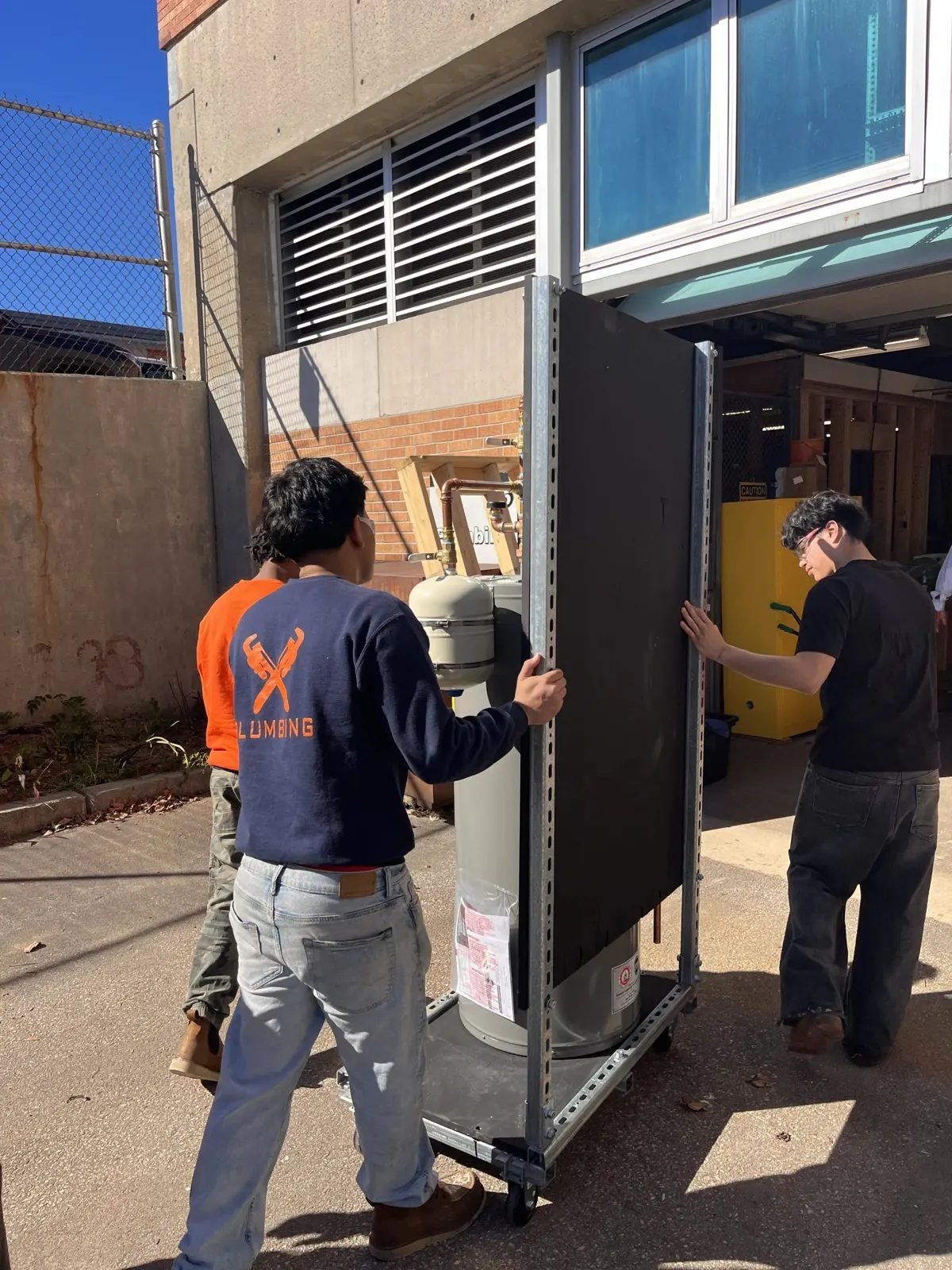 Three students wheel the finished training rig across the school yard