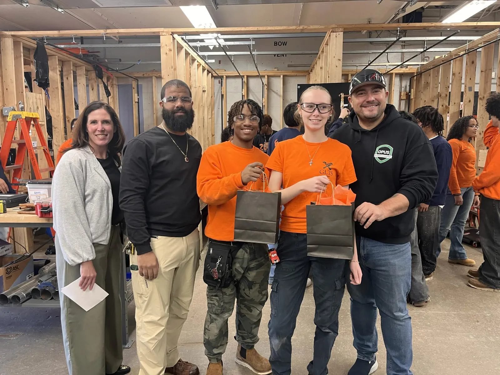 Two students receive gift bags from school staff and an Opus Plumbing & Heating representative