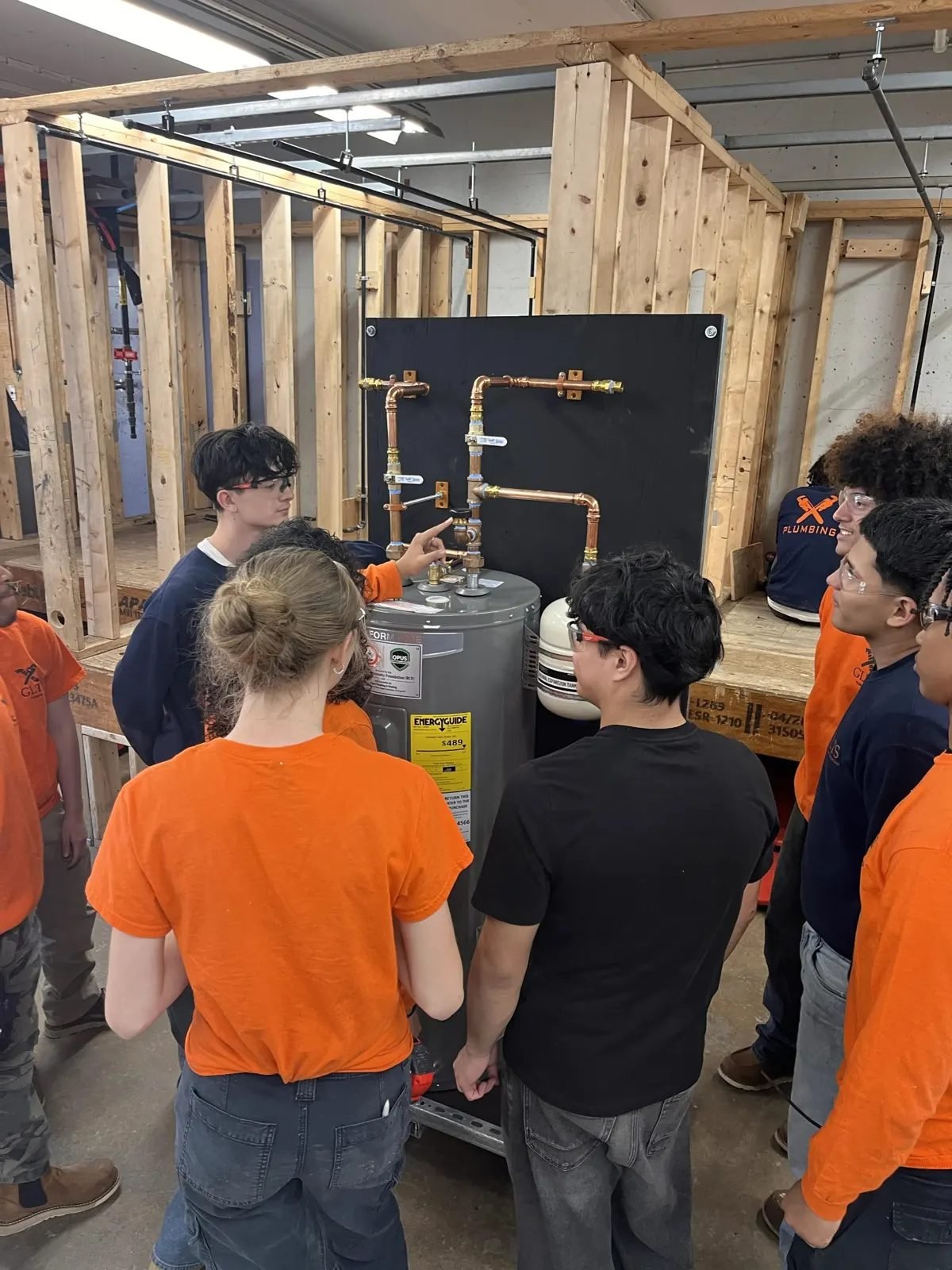 An instructor points out a valve on the water heater rig while students look on